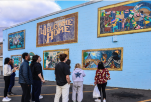 Elena Rosario Phd Candidate and First Year seminar students observing local artists’ murals (Tao LaBossiere, Camacho, Corey Pane, Samantha Jenkins, Che’ LaMora, Dwight Teal, Jr., Jackie Allen-Doucot and Joy Monroe) Titled “Welcome Home,” at Scott’s Jamaican Bakery in Hartford’s North End. 