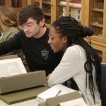 male and female student looking at rare books in Watkinson Library seminar room