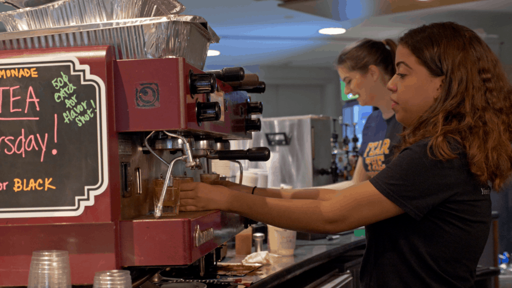 Two students prepare coffee drinks at an espresso machine