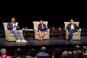 Three people sitting in chairs on stage during a panel discussion