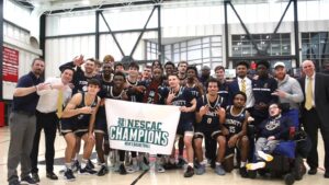 Men's basketball team on the court holding the 2026 NESCAC Champions banner