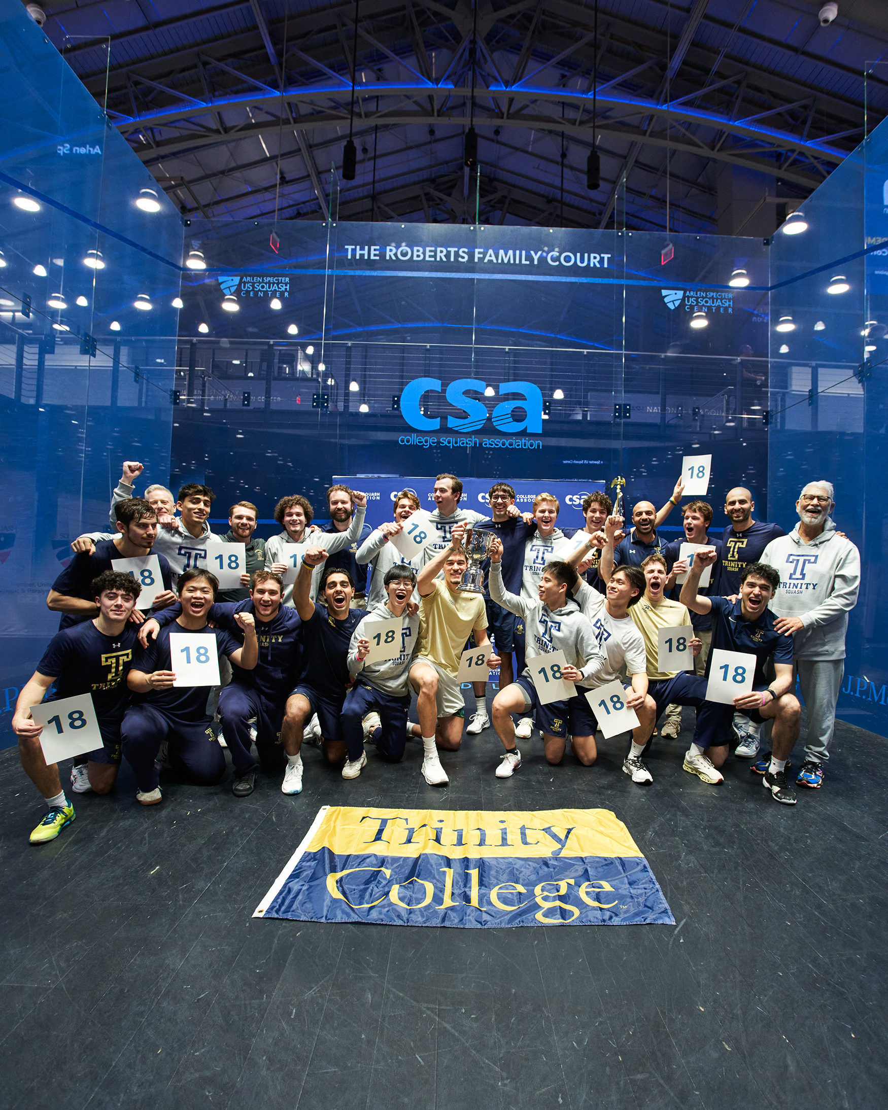 Men's squash team pose together holding signs that say "18"
