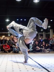 A break dancer on one arm and legs in the air wearing a grey sweat suit