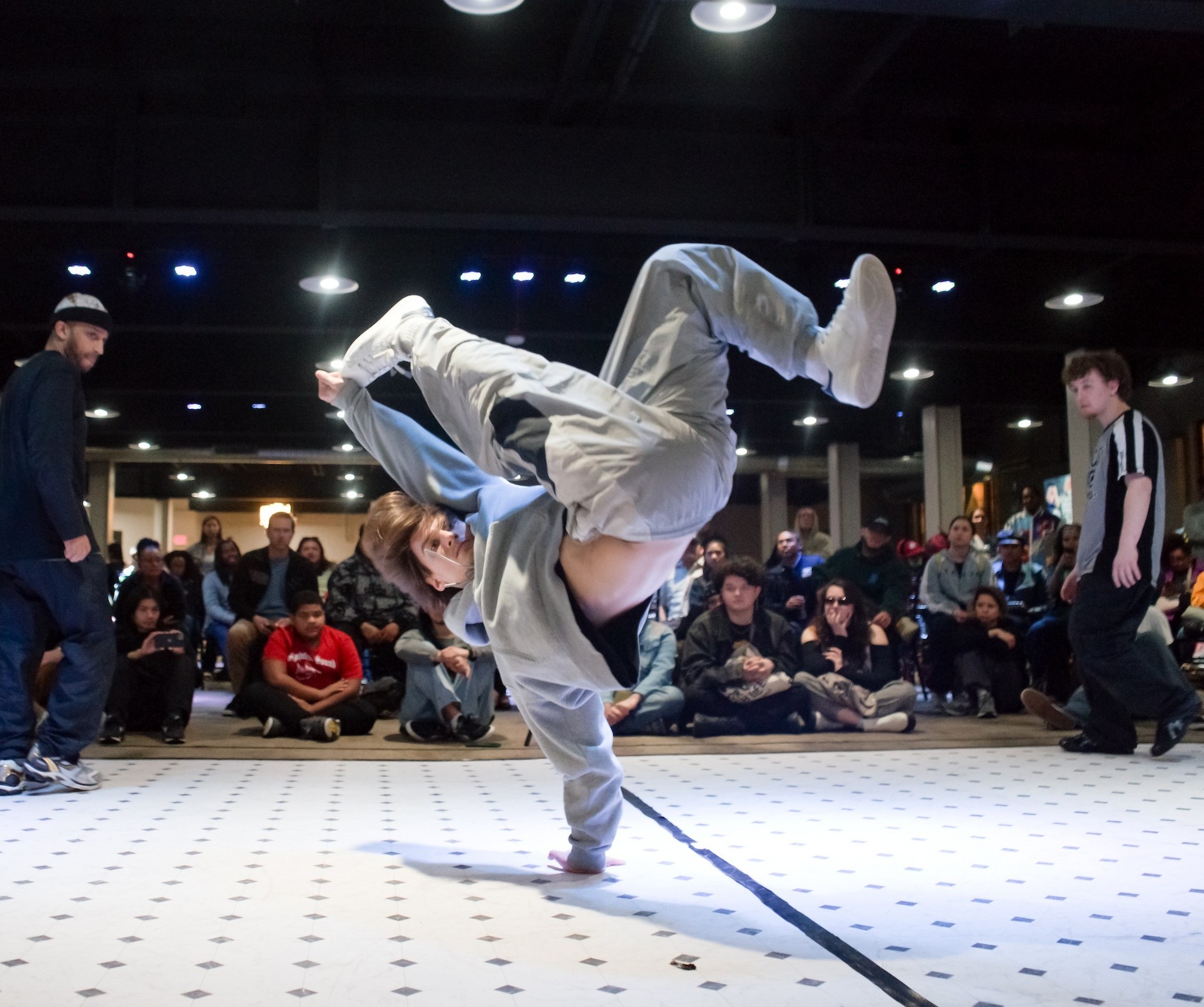 A break dancer on one arm and legs in the air wearing a grey sweat suit