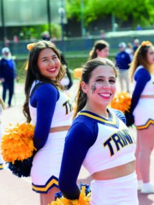 Trinity cheerleaders on the sidelines at a football game smiling at the photographer